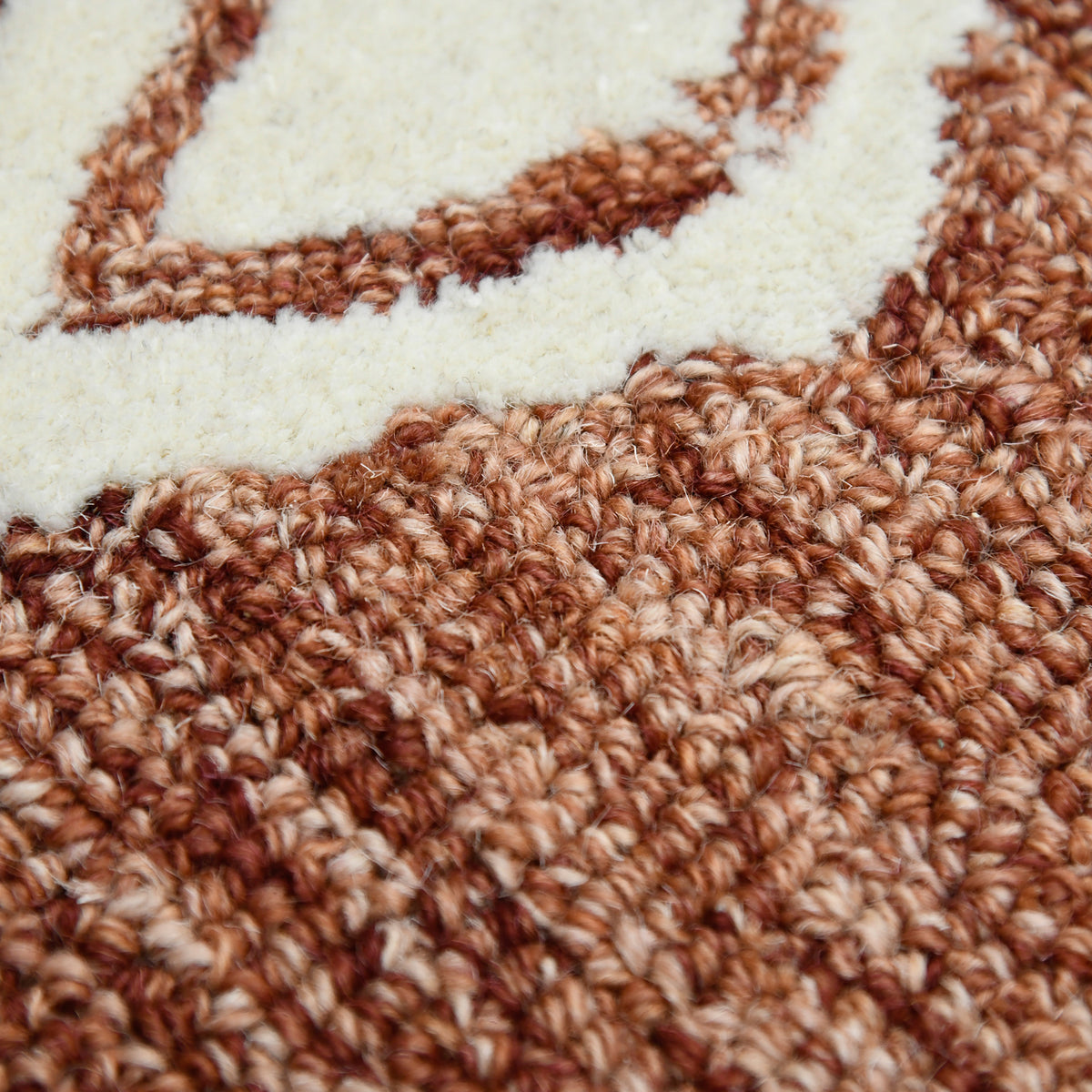 Close-up of rust rug pile showing hand-hooked loops and cream line pattern