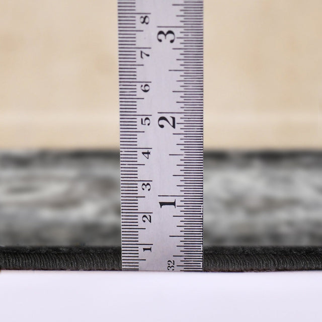 Measuring the low-pile height of a black and ivory area rug edge with ruler
