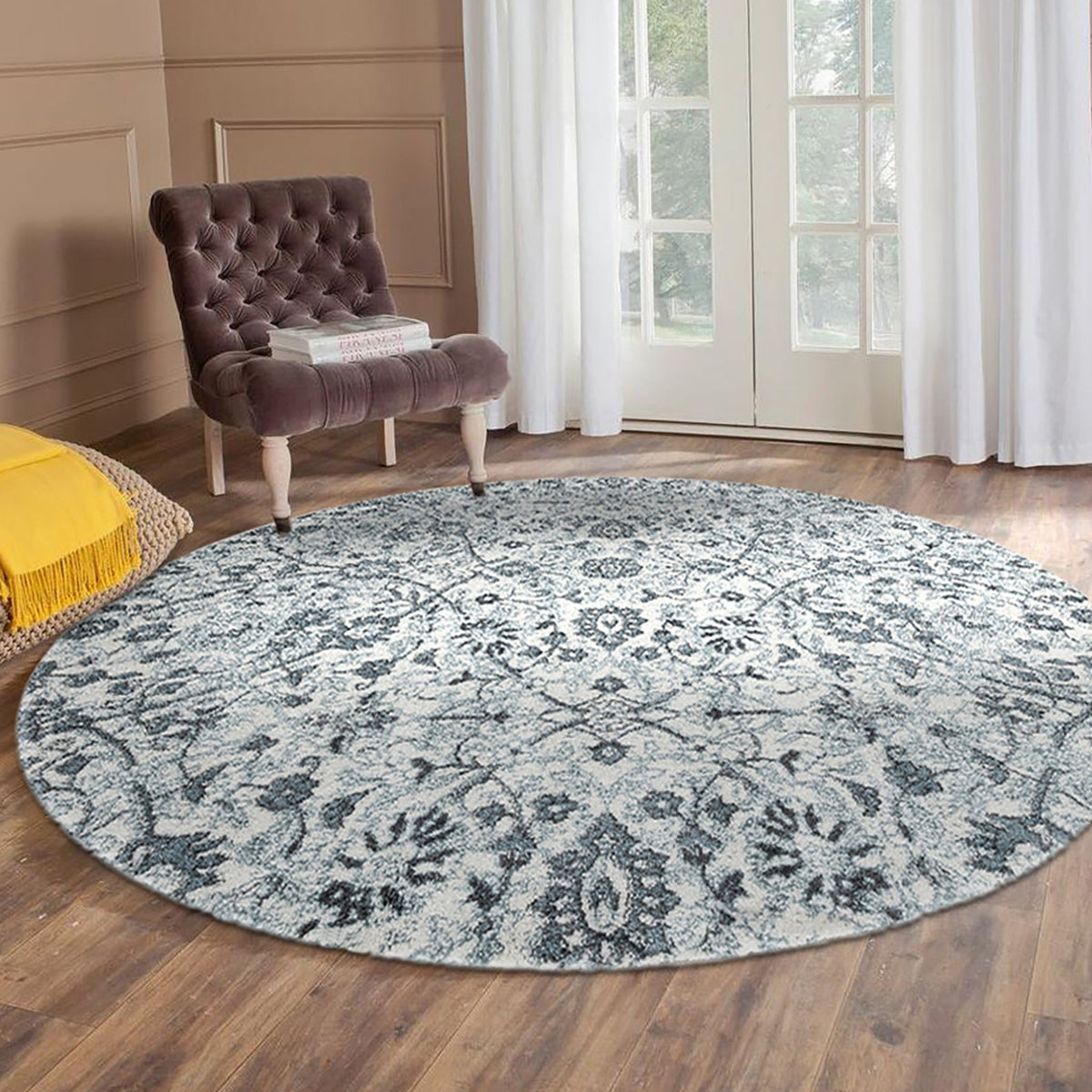 Light blue round floral area rug with ornate damask pattern in front of armchair