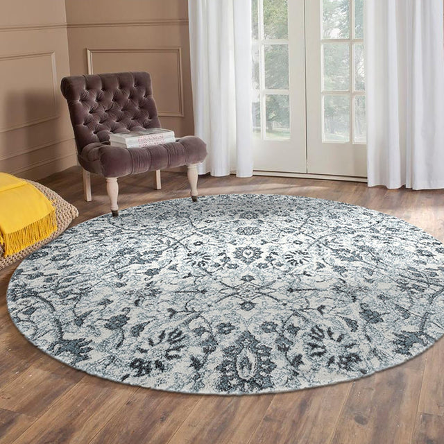 Light blue round floral area rug with ornate damask pattern in front of armchair