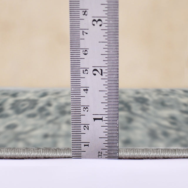 Light blue area rug edge with tape measure showing low pile height