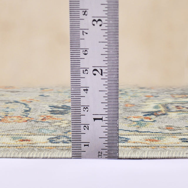 Gray bohemian floral area rug edge with tape measure showing rug thickness
