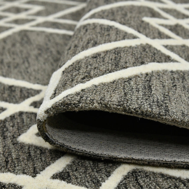 Hand-hooked area rug corner with raised texture and off-white geometric trellis lines.