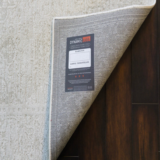 Ivory and grey power loomed traditional rug, visible woven edge and corner.