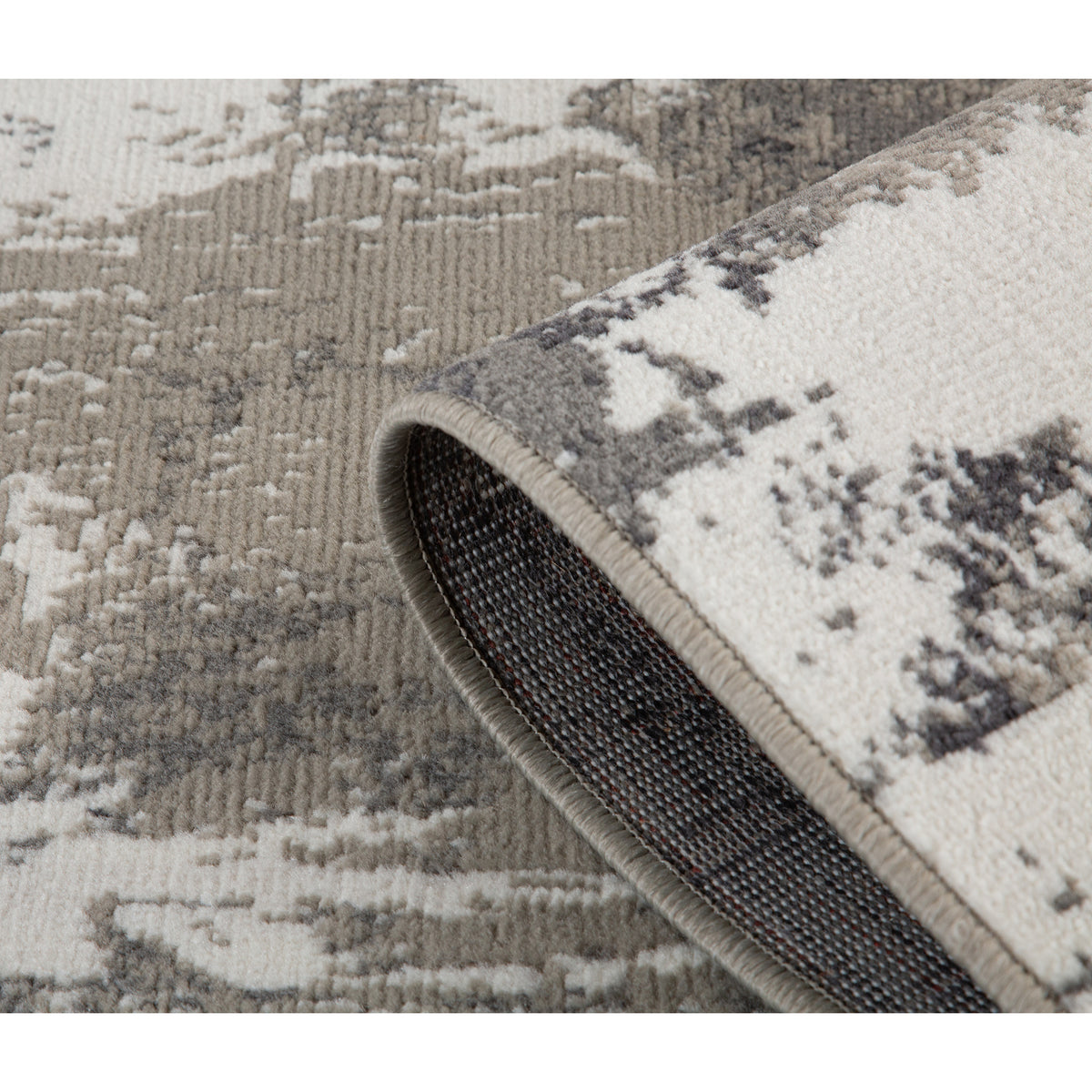 Rug edge detail showing thickness, folded corner, and dark backing under abstract design.
