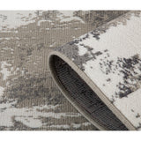 Rug edge detail showing thickness, folded corner, and dark backing under abstract design.