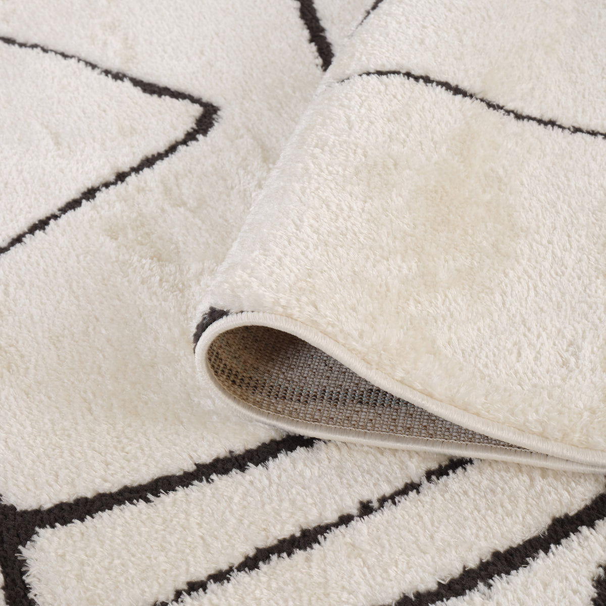 Ivory area rug with black motif and visible gray backing at lifted corner