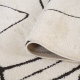 Ivory area rug with black motif and visible gray backing at lifted corner