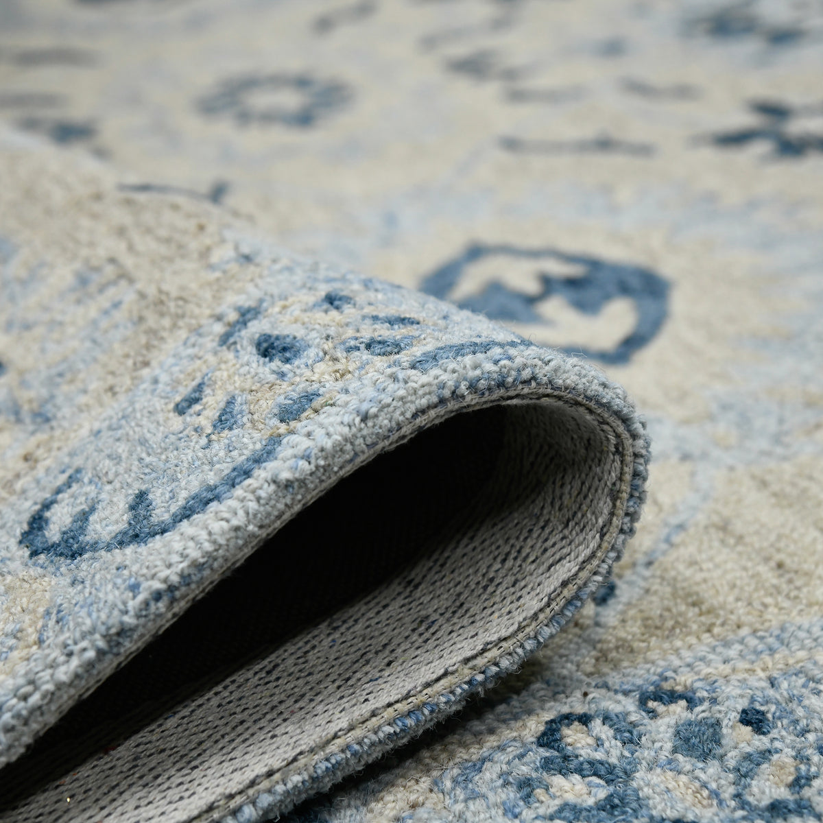 Rolled edge view of light blue floral rug underside with cream border and navy motifs