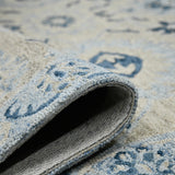Rolled edge view of light blue floral rug underside with cream border and navy motifs