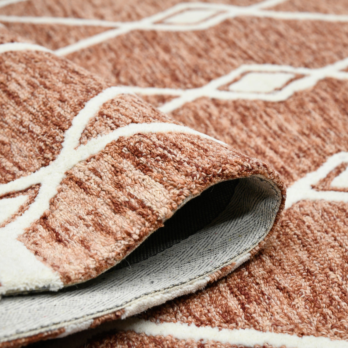 Rust geometric rug with cream border and visible underside backing at lifted corner
