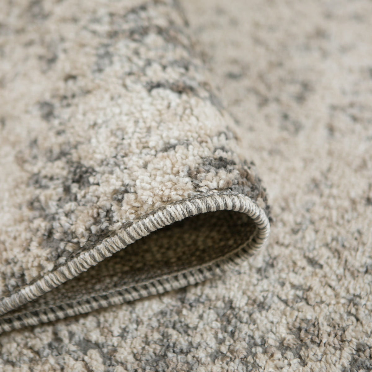 Close-up of rug edge showing dark backing and stitched border on gray/beige pile.