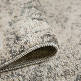 Close-up of rug edge showing dark backing and stitched border on gray/beige pile.