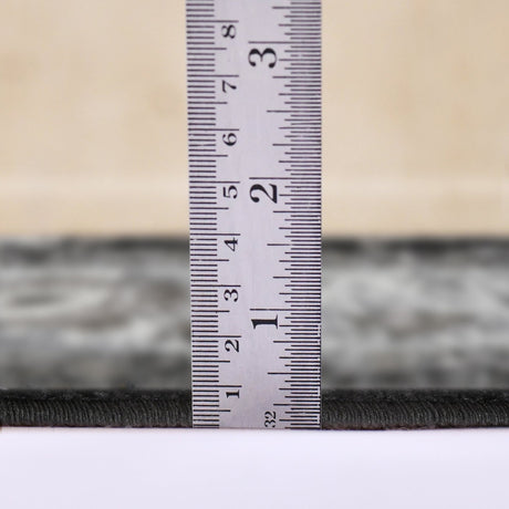 Measuring the low-pile height of a black and ivory area rug edge with ruler
