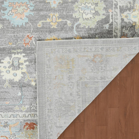 Taupe area rug with decorative border; dense geometric motifs in orange, blue, and yellow.