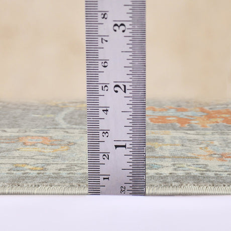 Taupe rug edge with visible binding; tape measure shows rug thickness/height.