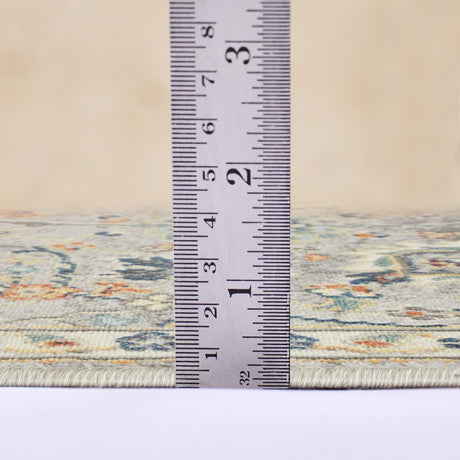 Gray bohemian floral area rug edge with tape measure showing rug thickness