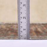 Taupe area rug thickness measured at edge with tape ruler, textured surface