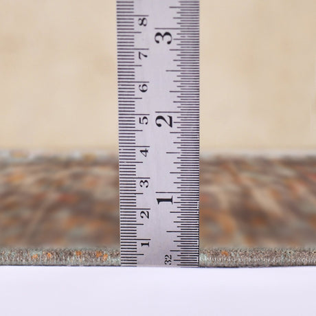 Taupe area rug thickness measured at edge with tape ruler, textured surface