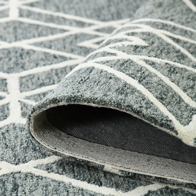 Edge curl close-up: gray rug underside with off-white bordered geometric motif