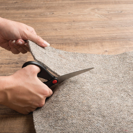 Grey rug pad being trimmed to fit with scissors, textured underside visible
