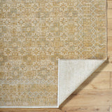 Handmade rug corner with geometric motif and light backing, in gold and beige tones.
