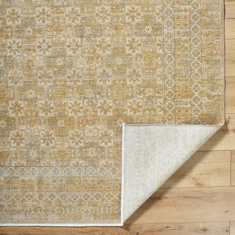 Handmade rug corner with geometric motif and light backing, in gold and beige tones.